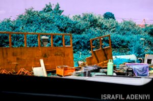Colour-shifted image of industrial waste materials. Metal poles, cannisters, brick in front of foliage.