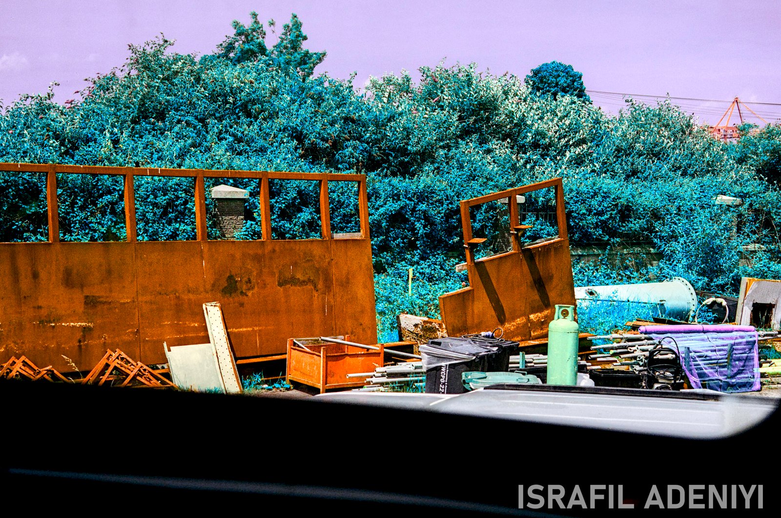 Remains of Industry Colour-shifted image of industrial waste materials. Metal poles, cannisters, brick in front of foliage.
