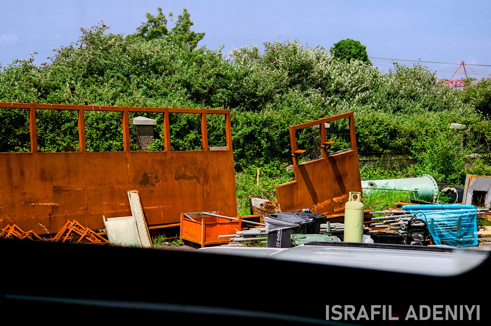 Remains of Industry Industrial waste materials. Metal poles, cannisters, brick in front of foliage.