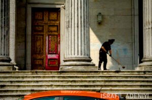 A person sweeping at the top of the steps of an official building.